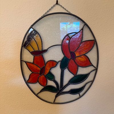 Oval stained glass suncatcher featuring vibrant red flowers and a yellow butterfly set against textured clear glass.