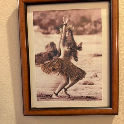 Framed vintage-style photograph depicting a Hawaiian hula dancer on a beach, set in a dark wood frame with off-white matting.