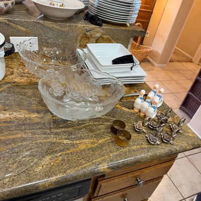 Assorted tableware featuring embossed floral glass serving bowls, white ceramic plates, patterned bowls, and small goose-shaped figurines...