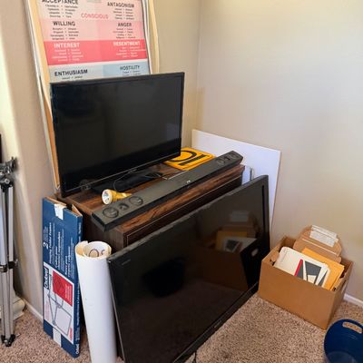 Collection of electronics and household items including flat-screen televisions, an LG soundbar, framed poster art, and office supplies...