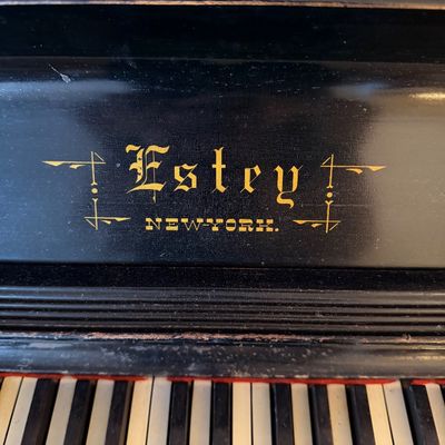 Close-up detail of an antique Estey New York piano, featuring gold lettering above the keyboard.