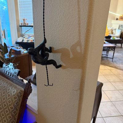 Modern dark bronze-finished climbing man wall sculpture attached to a twisted metal strand.