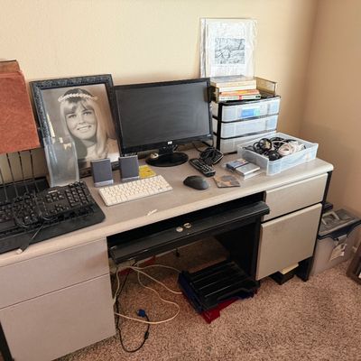 Contemporary office desk setup featuring a black HP computer monitor, dual keyboards, small computer speakers, plastic storage drawers,...
