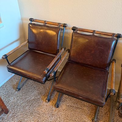 Pair of vintage campaign-style folding armchairs with dark brown leather upholstery, metal frames, and wooden armrests.