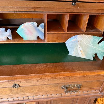 Set of three carved fluorite or onyx fish figurines displayed inside a wooden roll-top desk with a green writing surface.