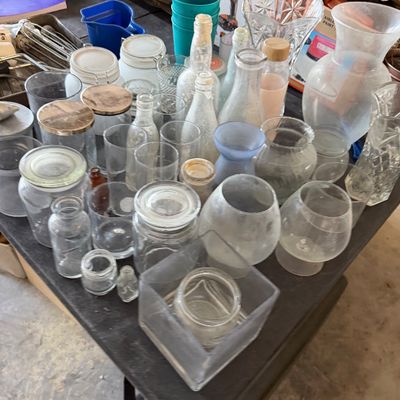 Large assortment of glassware and household items, including storage jars, vases, drinking glasses, and power tool boxes arranged on a...