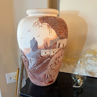 Large Southwestern sgraffito pottery vase featuring raised relief desert landscape motifs in earth tones, sitting beside a clear glass...