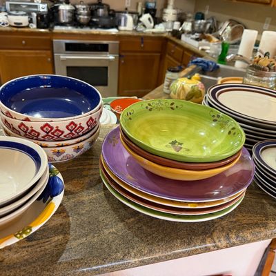 Assortment of colorful ceramic dishware, including stacks of bowls, plates, and mugs, displayed on a kitchen counter.