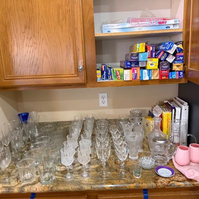 Large collection of crystal glassware, stemware, and barware displayed on a countertop below oak kitchen cabinets filled with household...