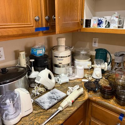 Collection of small kitchen appliances, including a slow cooker, juicers, hand mixers, electric knife, and food processors on a countertop.