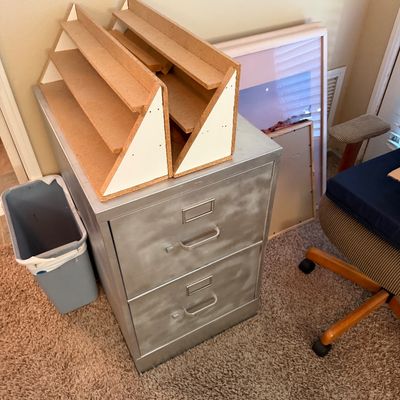 Two-drawer brushed metal filing cabinet with a pair of particle board tabletop display shelves sitting on top.