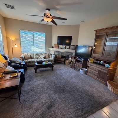 Living room setup featuring a carved wooden hutch, a floral upholstered sofa, recliners, tables, lamps, and televisions.