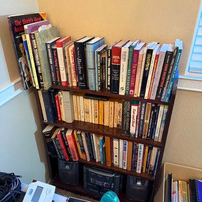Four-tier dark wood bookshelf filled with various hardcover and paperback books, including health, anatomy, and fiction titles.