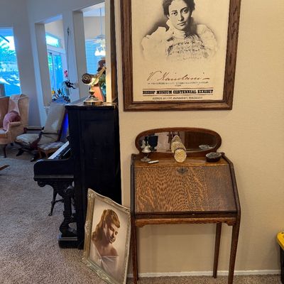 Antique tiger oak slant-top secretary desk with oval mirror top, alongside a framed Princess Kaiulani Bishop Museum poster and framed...