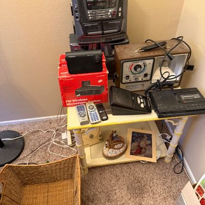 Collection of vintage electronics arranged on a small two-tiered table, including an Aiwa stereo system, Realistic FM wireless microphone...