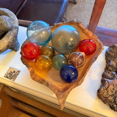 Collection of colorful vintage glass fishing floats displayed in a live-edge bark wood bowl.