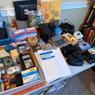 Assorted office and electronics supplies including cameras, calculators, microcassette recorders, stationary, and clipboards displayed on...