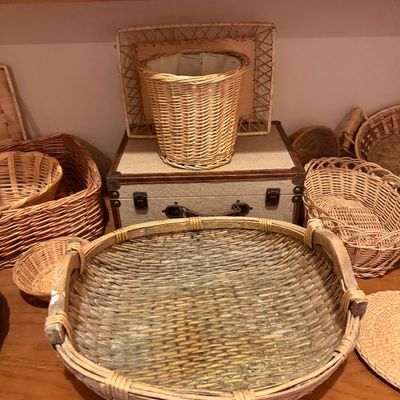 Collection of woven wicker and rattan baskets in various shapes and sizes alongside a vintage fabric-covered trunk.