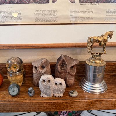 Collection of carved owl figurines in wood and stone, alongside a vintage brass horse trophy on a tiered metal base, displayed on a...