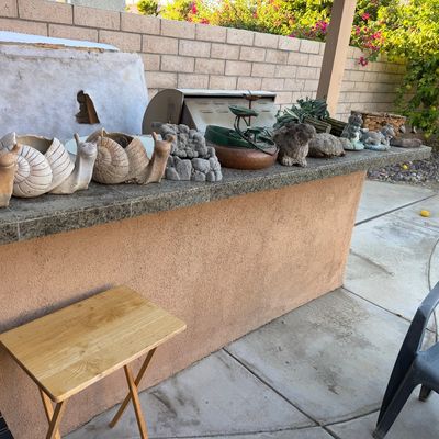 Collection of outdoor garden decor displayed on a patio counter, including snail-shaped planters, stone animal figurines, and tabletop...