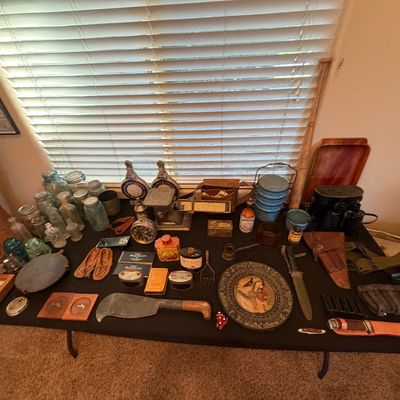 Collection of vintage collectables and militaria arranged on a table, including glass jars, insulators, knives, binoculars, leather...