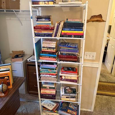 Tall white wire rolling bookcase fully stocked with a variety of vintage and modern paperback and hardcover books.