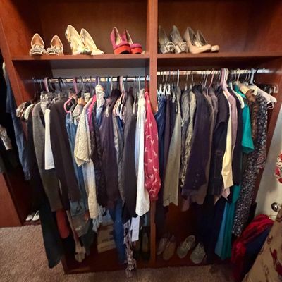 A wooden closet unit filled with women's clothing on hangers and various high-heeled shoes displayed on the top shelves.