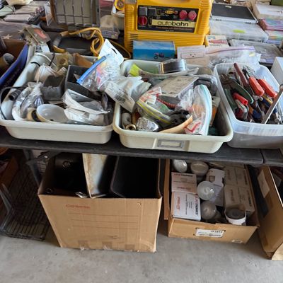 A table arranged with assorted tools, work lights, an Autobahn portable power station, and storage bins filled with hardware supplies.