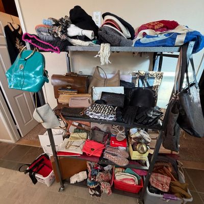 Metal rolling utility rack loaded with various women's handbags, scarves, shoes, and winter accessories.