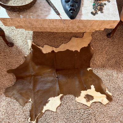 Small brown and white cowhide rug laid on carpet below a low table displaying woven baskets, a decorative face mask, and trinkets.