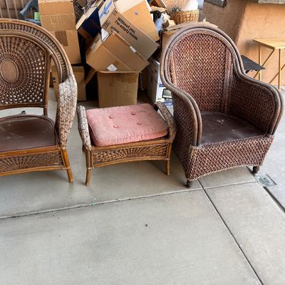 Vintage wicker patio seating set including two barrel-back armchairs and a matching footstool with a pink cushion.