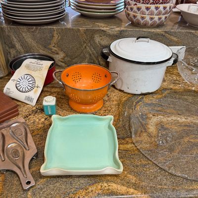 Assorted vintage kitchenware display including an orange enamel colander, a white enamel stock pot with lid, ceramic serving bowls, and...