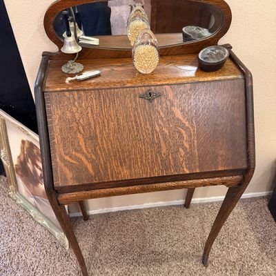 Antique tiger oak drop-front secretary desk featuring an attached oval mirror, cabriole legs, and decorative metal escutcheon, topped...