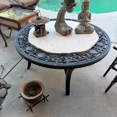 Black metal outdoor coffee table topped with decorative garden statues including a stone pagoda lantern and a seated Buddha figure.