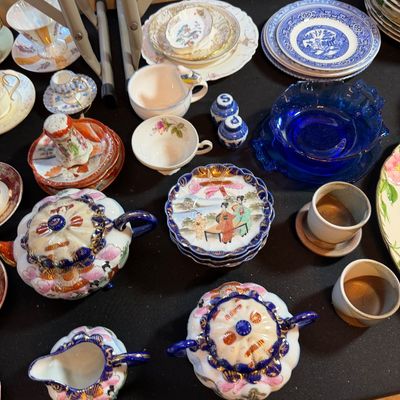 Collection of vintage porcelain and glassware, featuring Japanese Satsuma style teapots, saucers, blue Willow pattern plates, and cobalt...