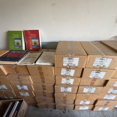 Large collection of sealed cardboard shipping boxes stacked alongside softcover self-help and Qigong books.