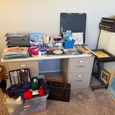 Crafting station set up on a metal double-pedestal office desk, surrounded by organized sewing, knitting, and art supplies including...