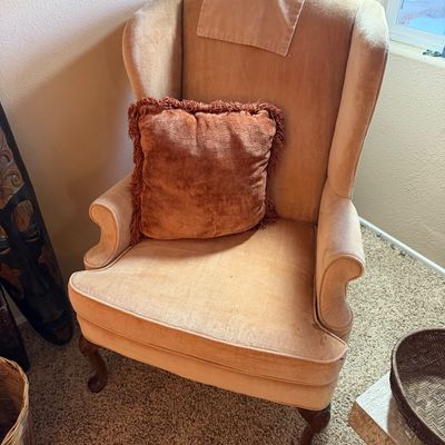 Vintage Queen Anne style wingback armchair upholstered in light peach velvet, featuring cabriole legs and a matching throw pillow with...