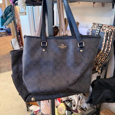 Coach tote bag featuring charcoal dark brown signature C canvas with black leather straps and gold-tone hardware. Shown hanging alongside...