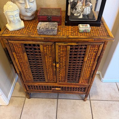Woven bamboo and rattan cabinet displaying various decorative Asian collectibles, including Buddha head sculptures and a encased Japanese...