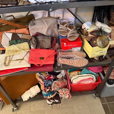 A collection of women's accessories displayed on metal shelving, including various leather handbags, clutches, scarves, belts, and...