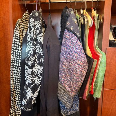 Collection of vintage women's clothing, including patterned jackets, vests, and a quilted coat, hanging in a wooden closet.