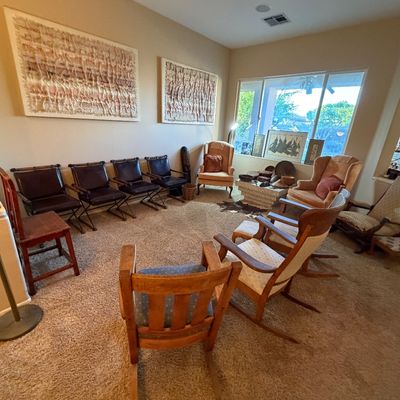 Living room setup featuring a collection of vintage seating including leather director-style chairs, wooden rocking chairs, wingback...