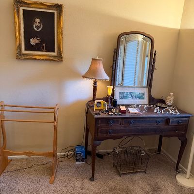 Vintage dark wood vanity with swivel mirror and matching cabriole legs, paired with a wooden quilt rack and framed art.