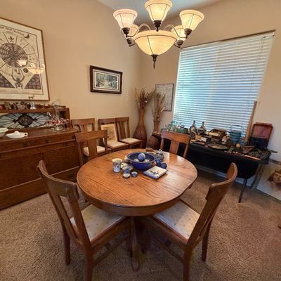 Round oak dining table with four matching chairs set beneath a frosted glass chandelier, accompanied by an oak buffet server and wall art.