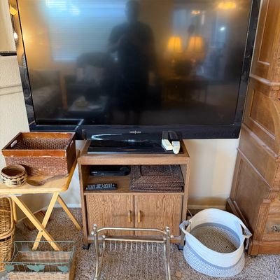 Insignia flat-screen television resting on a wood veneer media stand, flanked by various woven storage baskets and a metal magazine rack.