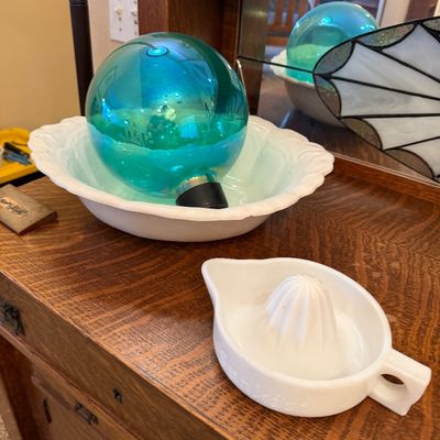 Vintage white milk glass citrus juicer alongside a teal glass witch ball resting in a matching milk glass bowl, displayed on a wooden...
