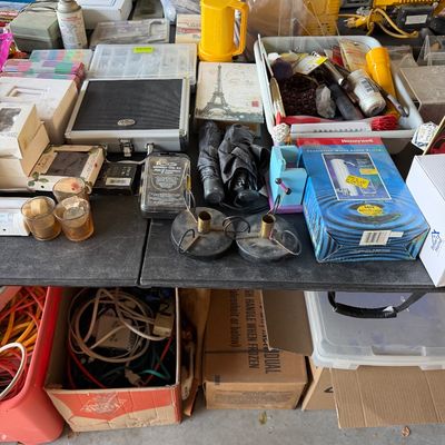 Assorted household goods and workshop supplies displayed on a folding table, including a Honeywell countertop water filter, small hand...