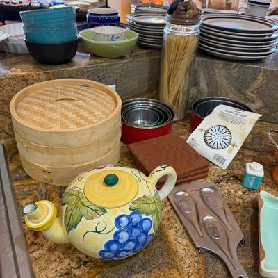 A collection of kitchen items including a hand-painted ceramic teapot with grape motifs, a wooden bamboo steamer set, stacked ceramic...