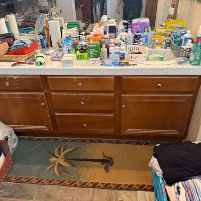 Large wooden double-basin bathroom vanity, filled with assorted toiletries, medications, and personal care items.